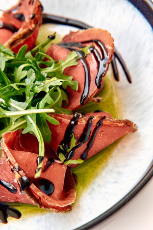 A Delicious Plate of Sliced Beef with Fresh Arugula and Balsamic Drizzle Artfully Arranged in a...