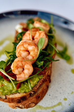 A Delicious Plate of Toast Topped with Avocado, Shrimp, and Fresh Greens, Perfect for a Light Meal or Appetizer on a Sophisticated Dining Table.の写真素材