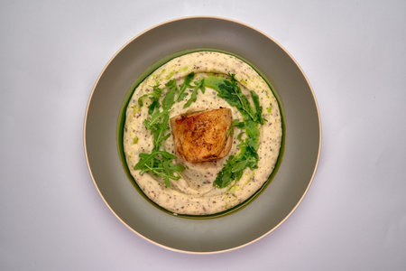 A Beautifully Plated Dish Featuring Seared Fish on a Creamy Mousseline and Garnished with Fresh Arugula for an Elegant Culinary Presentationの写真素材