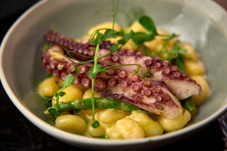 A Delectable Dish Featuring Octopus with Gnocchi and Fresh Green Beans Served in a Stylish Bowl, Garnished with Microgreens for an Elegant Presentationの写真素材