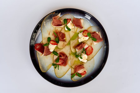 Deliciously Crafted Gourmet Dish Featuring Delicate Slices of Prosciutto with Fresh Strawberries and Creamy Cheese on a Stylish Plateの写真素材