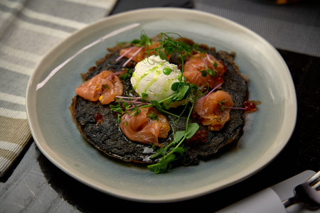 Delicious Gourmet Dish Featuring Black Crepe with Smoked Salmon, Fresh Herbs, and Creamy Dollop of Whipped Cheese on a Stylish Plateの写真素材