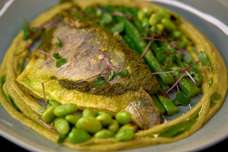 Flavorful Dish Featuring Herb-Crusted Fish Served on a Bed of Pureed Greens with Fresh Vegetables and Garnished with Microgreens for an Exquisite Presentationの写真素材