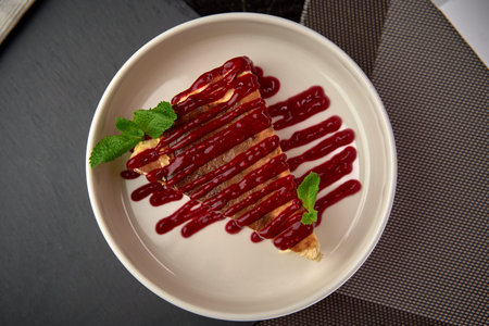 A Delicious Slice of Cake Topped with Rich Berry Sauce and Fresh Mint Leaves Perfectly Arranged on a...