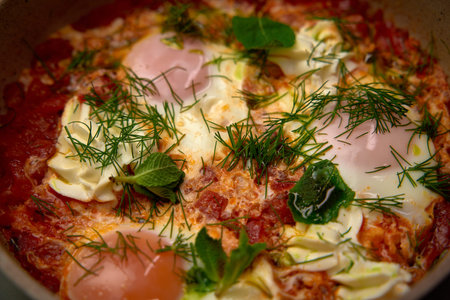A Delicious Dish of Shakshuka Featuring Poached Eggs in a Spicy Tomato Sauce Garnished with Fresh Herbs and Vegetables for a Flavorful Mealの写真素材