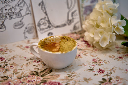 A Delicate Cup of Coffee Topped with a Beautiful Layer of Sweet Cream and adorned by Fresh Flowers on a Soft Floral Tableclothの写真素材