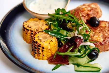 A Vibrant Culinary Presentation featuring Grilled Corn, Fresh Greens, and Savory Protein Served with a Creamy Dip on an Elegant Plateの写真素材