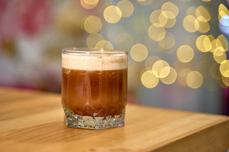 A delicious cocktail in a crystal glass, elegantly placed on a wooden table, shimmering bokeh lights in the background create a festive atmosphere.の写真素材