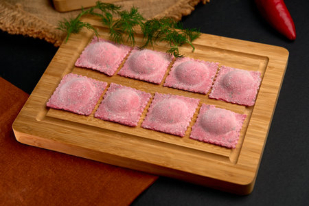 Delicate handmade pink ravioli arranged on a wooden platter with a rustic background, showcasing culinary artistry in preparation for a gourmet dish.の写真素材