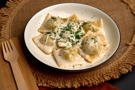 Delicious Plate of Homemade Ravioli Topped with Creamy Sauce and Fresh Herbs Served on Rustic Tableware for a Hearty Italian Mealの写真素材