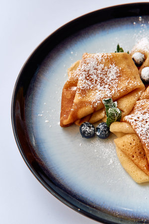Deliciously Arranged Pancakes Topped with Powdered Sugar, Fresh Blueberries, and Mint Leaves on a...