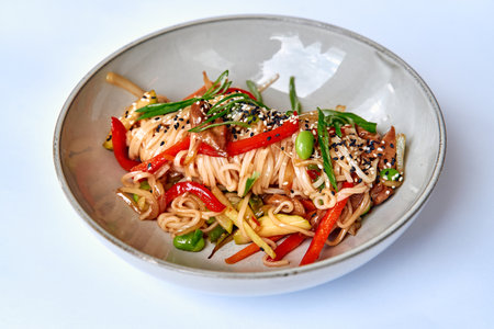 A Colorful Bowl of Stir-Fried Noodles with Vibrant Vegetables, Perfectly Garnished with Sesame Seeds and Greens, Ideal for a Delicious Meal.の写真素材