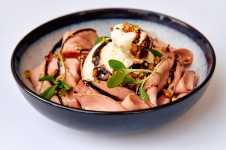 A Delicate Culinary Creation Featuring Slices of Savory Meat Accompanied by Creamy Cheese and Garnished with Nuts and Fresh Greenery in a Stylish Bowlの写真素材