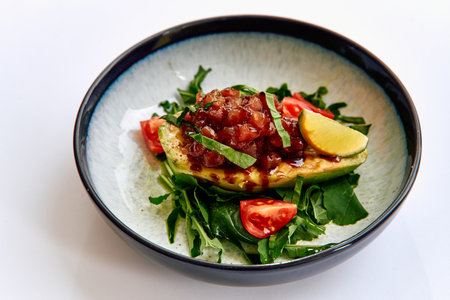 Deliciously Crafted Avocado Dish Served on a Bed of Fresh Greens with Tomatoes and Garnished with Zesty Lemon for a Flavorful Experienceの写真素材