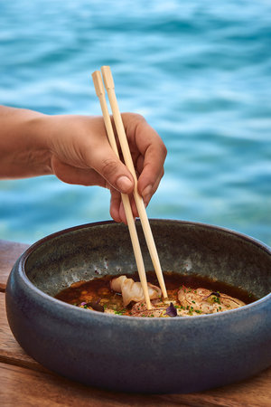 A Hand Gently Using Chopsticks to Enjoy a Delicate Dish by the Water, Showcasing the Art of Dining...