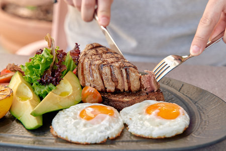 A Deliciously Cooked Steak Accompanied by Fried Eggs and Fresh Vegetables on a Stylish Plate in a...