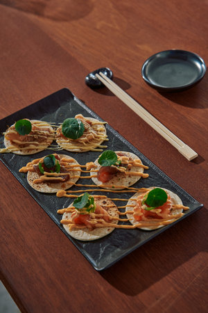 Deliciously arranged small tacos topped with flavorful ingredients, garnished with herbs, served elegantly on a black plate, perfect for culinary enthusiasts.の写真素材