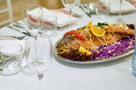 A beautifully presented whole fish dish garnished with vegetables and herbs, served on a silver...