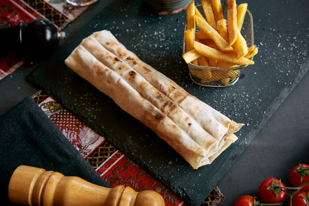 Deliciously Wrapped Flatbread with Savory Filling Served with Crispy Fries on a Rustic Slate...