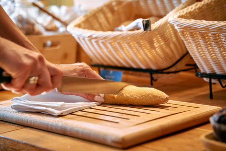 A Close-Up View of a Hand Slicing Fresh Bread on a Wooden Cutting Board Surrounded by Baskets,...
