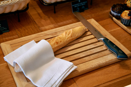 A Freshly Baked Baguette Resting on a Wooden Cutting Board Next to a Sharp Knife and Linen Napkin,...