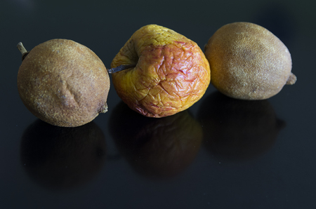 a shrunken apple between two aligned shriveled lemons are reflected on a dark backgroundの写真素材
