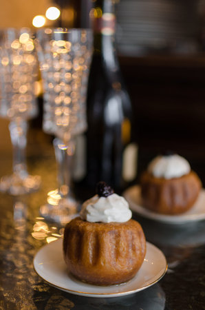 Festive meal with champagne, drinking glasses and a garland and rum baba soaked in sweet syrup stuffed with currants and cream for dessertの写真素材