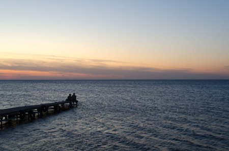 Two lovers sit at sunset on a pier in the Black Seaの写真素材