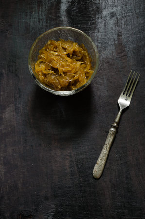 Homemade onion marmalade and fork on dark wooden background.の写真素材