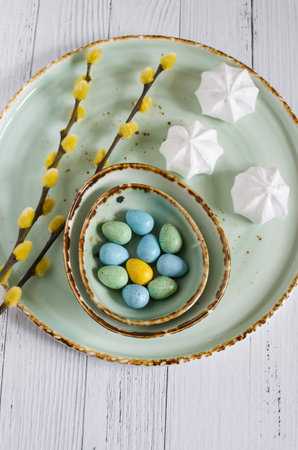 Easter composition - a plate with egg-shaped dragee candies, white meringues and willow branchesの写真素材