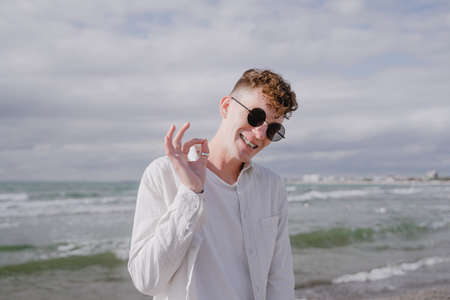 young guy in braces with round sunglasses at the sea shows okayの写真素材