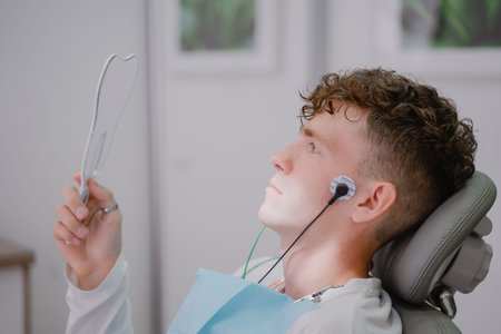 the patient sits in an orthodontist's chair during the tens procedure, looks in the mirror at the electrodes placed on the faceの写真素材