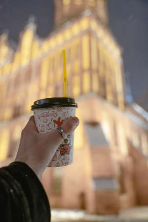 paper cup in a man's hand, holds against the background of urban architecture, a walk along the evening streetsの写真素材