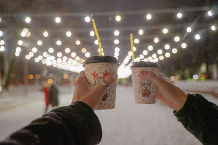 a walk in the winter, Christmas lights are on, paper cups with warming drinks are in handの写真素材