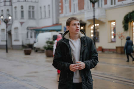 a young man with a questioning face, waiting for an answer, looks away, in a black winter jacket in an urban environmentの写真素材