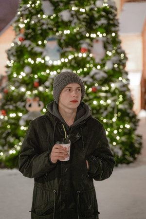 in cold winter drinks a hot drink by the Christmas tree, in winter clothes in an urban environment