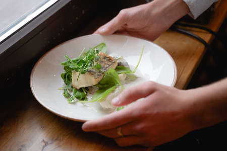 puts a plate of fish on a wooden table, beautiful restaurant serving decorated with herbsの写真素材