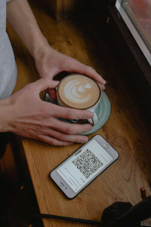 holding a cup of coffee with his hands next to a phone with an open code, new rules, cappuccino with a pictureの写真素材
