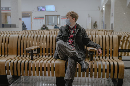 while waiting for his transport for travel, sitting at a train station, at an airport, wearing a...