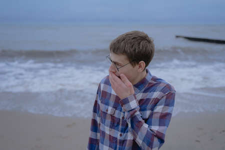teenager from surprise covered his mouth with his hand, stands on the seashore in a shirt and glasses for visionの写真素材