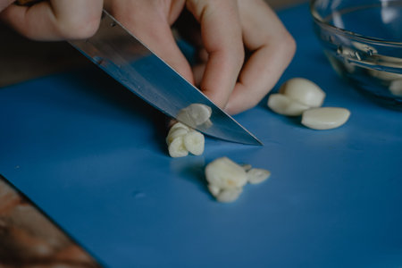 cuts garlic on a blue plate, with a kitchen knife, close-up, cooking homemade foodの写真素材