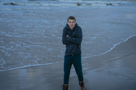 the guy is cold on the seashore, stands in a blue hoodie, warms his hands from frostの写真素材