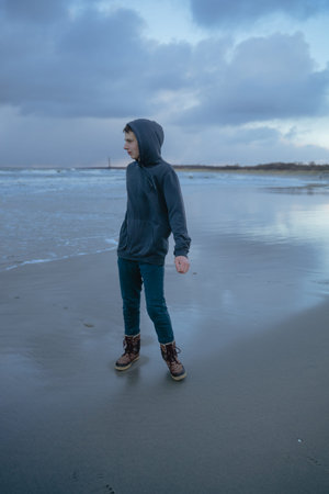a teenager with a pensive face stands on the shore, looks to the side, a young man in full growth,...