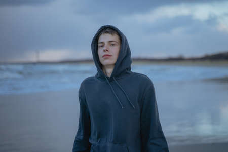 Handsome teenage boy in blue hoodie and hoodie standing outdoors against the background of the sea nature. Adolescence.の写真素材