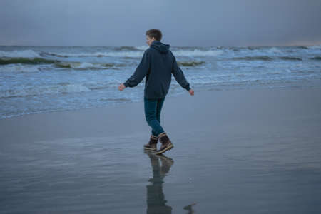 a young guy in a blue hoodie walks along the shore of a stormy seaの写真素材
