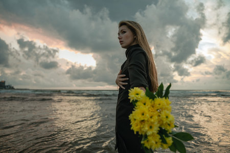 a girl with yellow flowers stands against a cloudy sky, rests on the sea with a bouquet of chrysanthemumsの写真素材