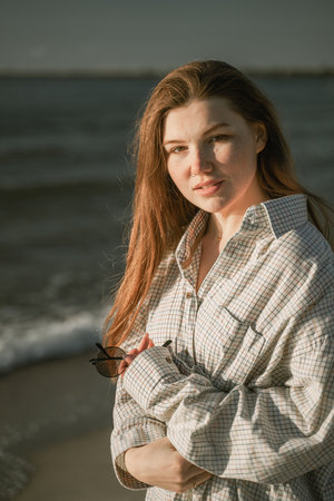 portrait of a woman with long red hair, looking at the camera on the seashore, on a bright sunny dayの写真素材