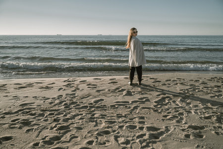 a girl stands on a sandy beach, by the sea, in a long shirtの写真素材