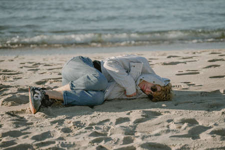 a homeless man lies on the sand, hid from the cold, a lonely guyの写真素材