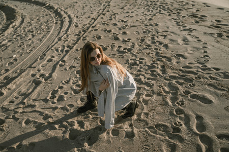 a woman sitting on a sandy beach looks away, wearing sunglasses, with long red hairの写真素材